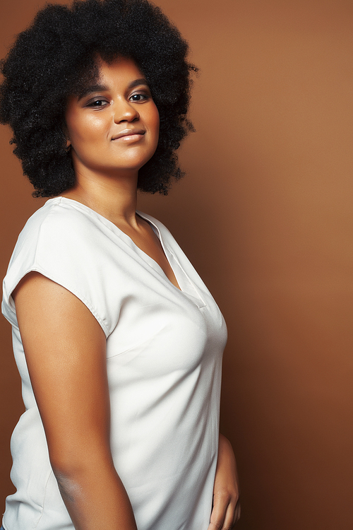 pretty young african american woman with curly hair posing cheerful gesturing on brown background, lifestyle people concept close up