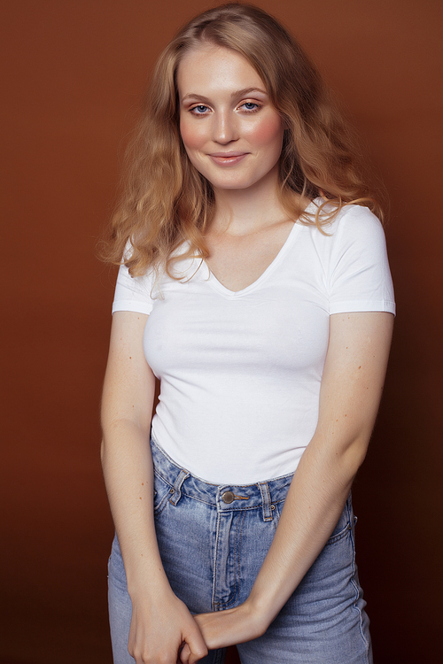 young pretty girl with blond curly hair posing cheerful on brown background, lifestyle people concept close up