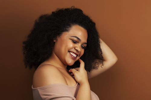 pretty young african american woman with curly hair posing cheerful gesturing on brown background, lifestyle people concept closeup