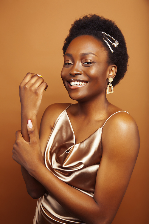 young pretty african model with golden jewelry in fashion style dress smiling happy on brown backround, lifestyle people concept close up