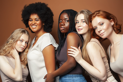 young pretty african and caucasian women posing cheerful together on brown background, lifestyle diverse nationality people concept closeup