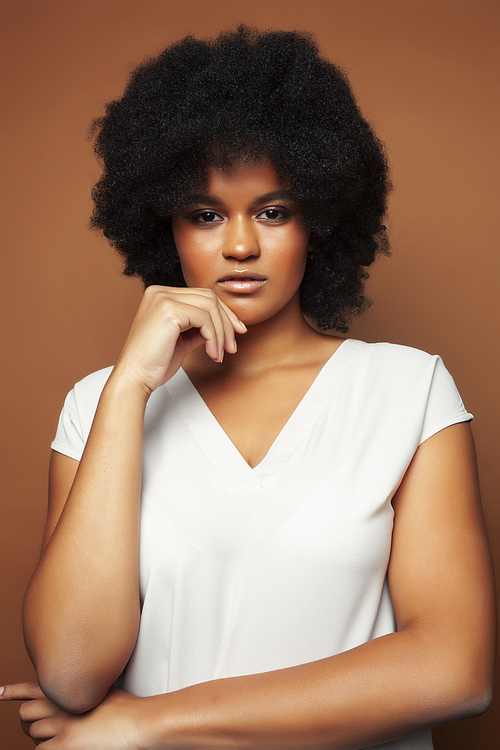 pretty young african american woman with curly hair posing cheerful gesturing on brown background, lifestyle people concept close up