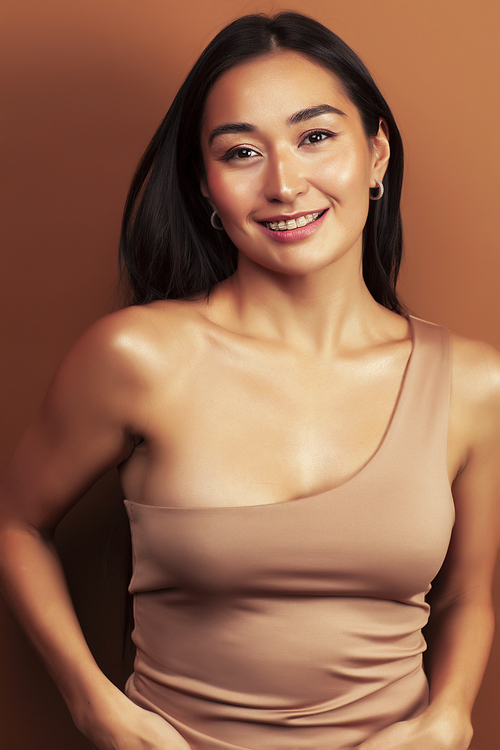 young pretty asian woman cheerful smiling posing on warm brown background, lifestyle people concept closeup