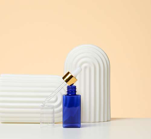 blue glass bottle with pipette stands on a beige background. Cosmetics SPA branding. Packaging for gel, serum, advertising and product promotion, mock up