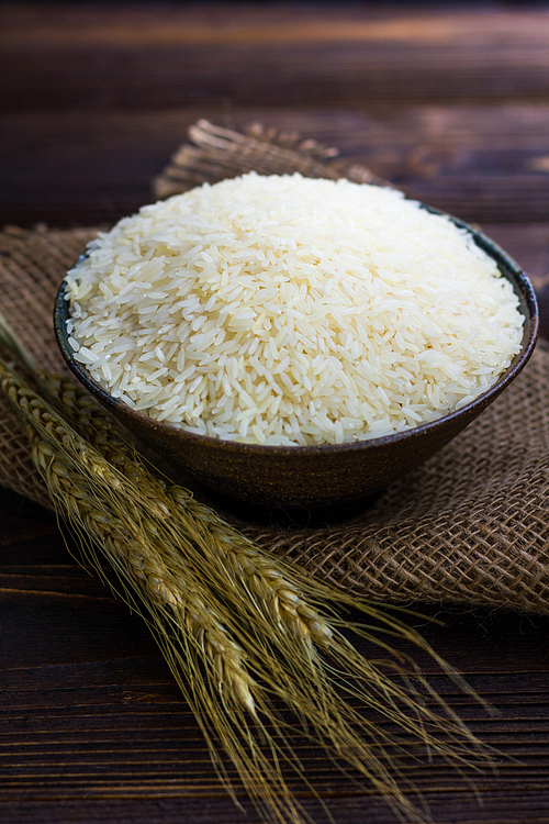 White rice in bowl and ear of paddy on wooden table.