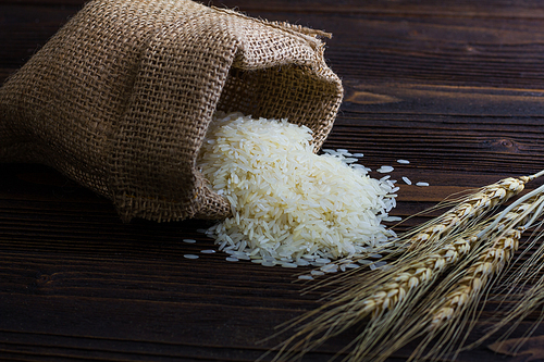 White rice in sack and ear of paddy on wooden table.