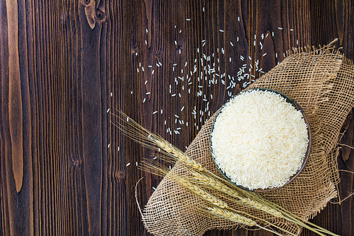 White rice in bowl and ear of paddy on wooden table.