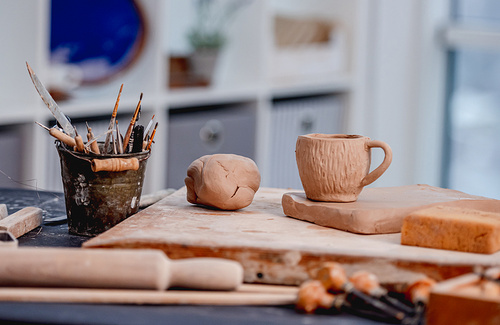 Pottery tools, cup and clay lying on table at workshop