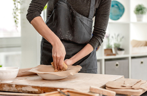 Woman using wet sponge for plate forming from clay at pottery workshop