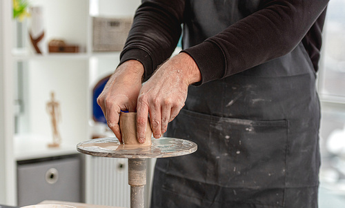 Man using pottery wheel for molding cup from clay at workshop