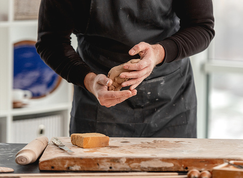 Man potter in apron molding clay in hands at workshop