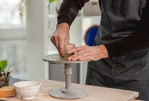 Man using pottery wheel for molding cup from clay at workshop