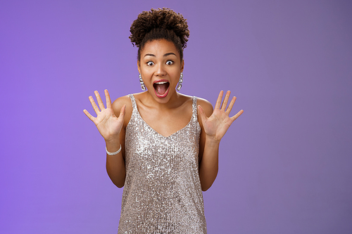 Shocked excited charming african-american woman in silver glittering dress raise palms amused screaming thrilled wondered widen eyes receive awesome incredible surprise, blue background.
