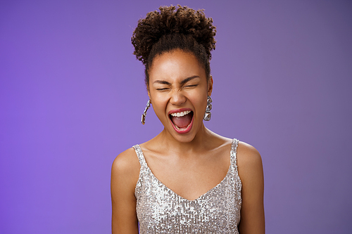 Joyful good-looking african-american stylish young woman in silver evening dress close eyes yawning sleepy tired party all night standing amused blue background wanna sleep. Copy space