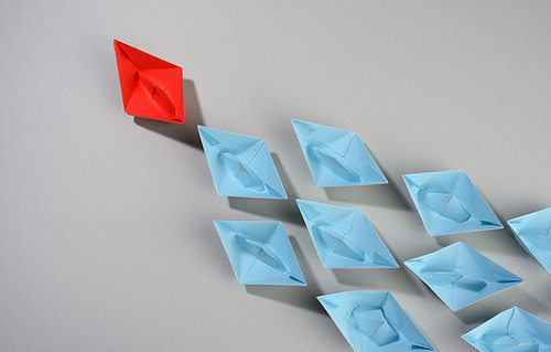 group of paper boats on a gray background. concept of a strong leader in a team, manipulation of the masses, following new perspectives, collaboration and unification. Startup