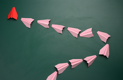 Group of pink paper airplanes following the first red on a green background. The concept of uniting a team to achieve goals, a strong leader, a highly effective group, coordination of actions