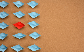 group of blue paper boats and one red in the middle on a brown background. The concept of a unique and extraordinary personality in a team. Talented employee, be yourself