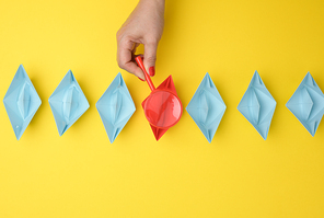 female hand holds a magnifying glass over a row of paper boats on a yellow background. Talent search concept, recruiting, recruitment interviews