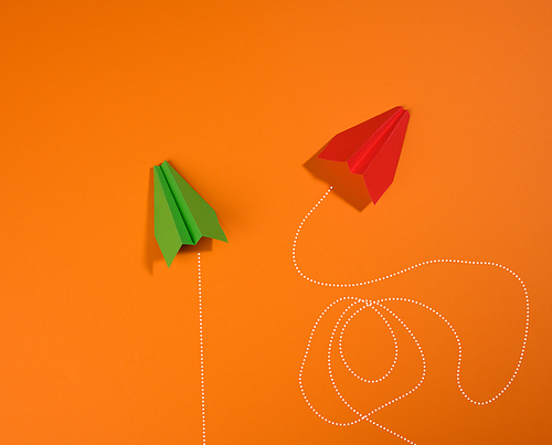 two paper airplanes with different trajectory of movement on an orange background, the concept of optimization, achievement of goals, extraordinary thinking. Complex things are simple