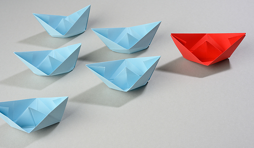 group of paper boats on a gray background. concept of a strong leader in a team, manipulation of the masses, following new perspectives, collaboration and unification. Startup