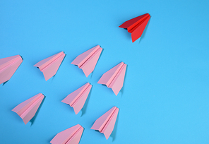 group of pink paper planes follow the first red against a blue background. The concept of uniting a team to achieve goals, a strong leader, a highly effective group, top view
