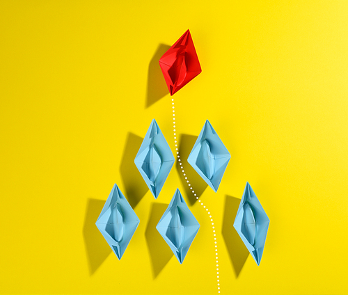 group of blue paper boats and one red led on a yellow background. Strong leader concept, growth of unique and talented employees, top view