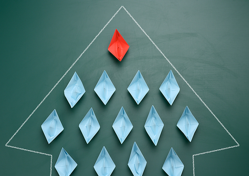 group of paper boats on a green background. concept of a strong leader in a team, manipulation of the masses, following new perspectives, collaboration and unification. Startup