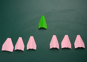 group of pink paper planes follow the first green airplane against a green background. The concept of uniting a team to achieve goals, strong leader, highly effective group, coordination of actions
