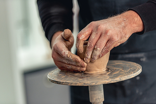 Man working on pottery wheel with clay at light workshop