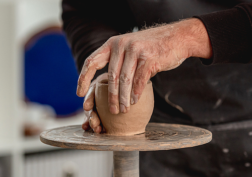 Man working on pottery wheel with clay at light workshop