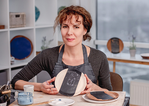 Woman showing finished handmade plate with pattern at studio
