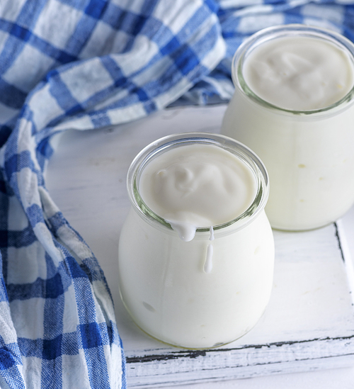 glass jars with homemade yogurt on a white wooden board,  top view