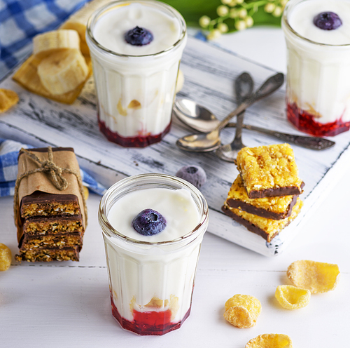 yogurt in transparent glass with syrup and banana on a white wooden background, top view