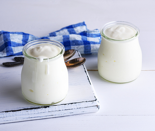 two glass jars with milk yoghurt homemade on a white wooden background