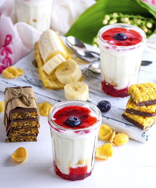 homemade yogurt in transparent glass with syrup and banana on a white wooden background, close up