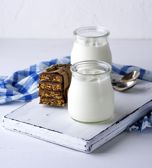 homemade yogurt in a glass jar and snacks on a white wooden board, close up