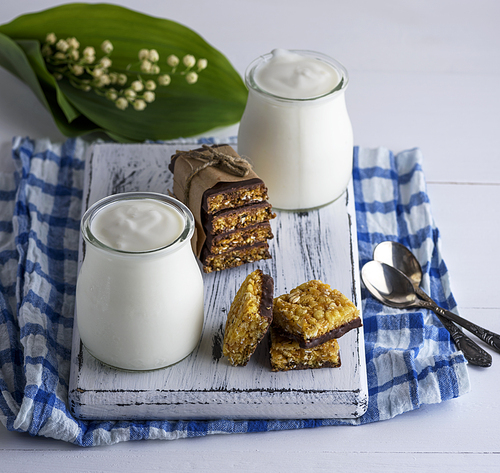 two jars with homemade yogurt and snacks from muesli on a white wooden board, top view