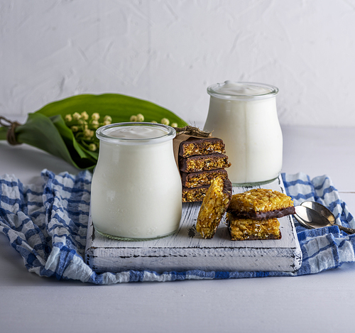 homemade yogurt in a glass jar and snacks on a white wooden board, close up