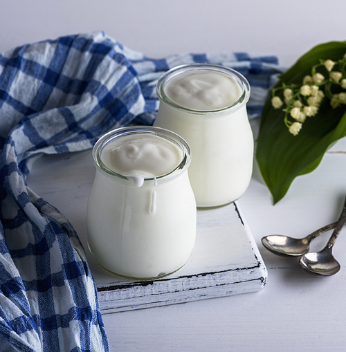 two glass jars with homemade yogurt on a white wooden board, top view