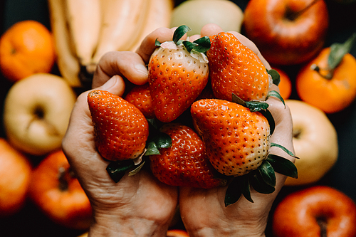 A vertical shot of two hands grabbing a bunch of strawberries over a bunch of vegetables