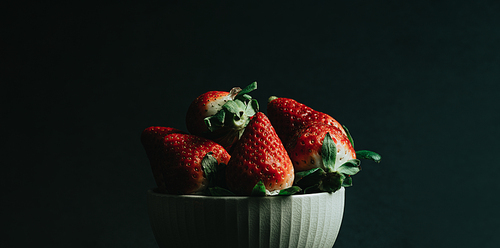 A minimal shot of a bunch of strawberries in a bowl over a dark background with copy space