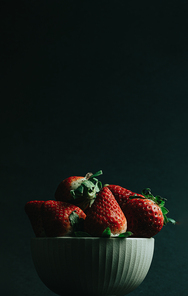 A minimal shot of a bunch of strawberries in a bowl over a dark background with copy space