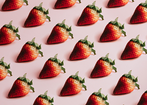 Minimal and repetitive pattern of delicious strawberries over a pastel pink background