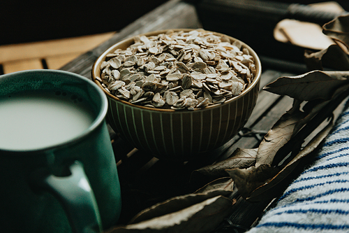 A close up of a bowl filled with oat seeds over a wooden table on moody tones