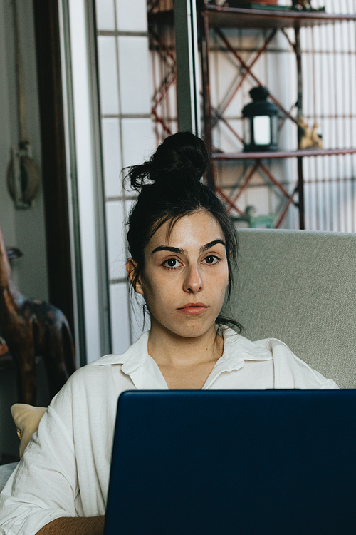 Young woman looking to camera while working on his laptop on the couch, portrait