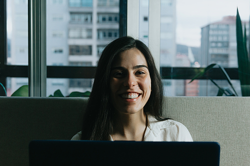 A close up portrait of a young woman smiling to camera while working from home