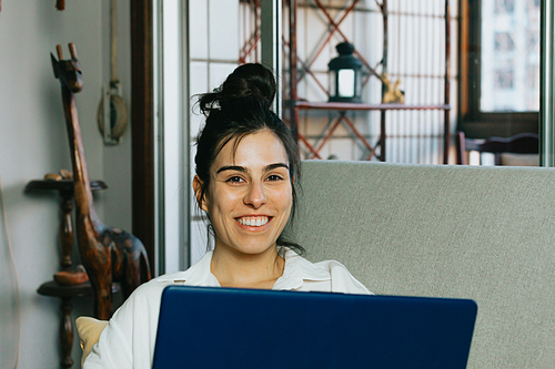 Young woman smiling to camera while working from home with the laptop