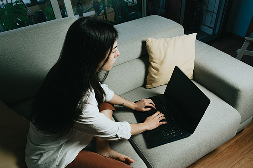 Top view of a young woman working on his laptop on the couch while working from home