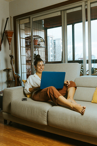 A woman working on his laptop while smiling at home during a bright home