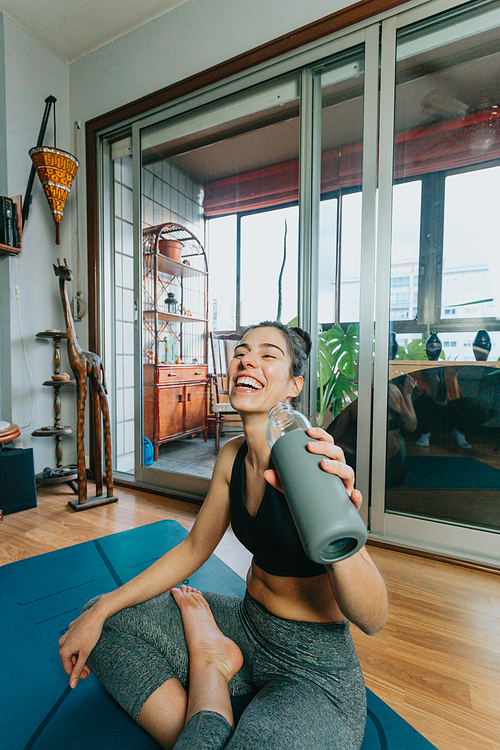 A young woman smiling to camera while drinking water doing fitness and yoga at home with copy space